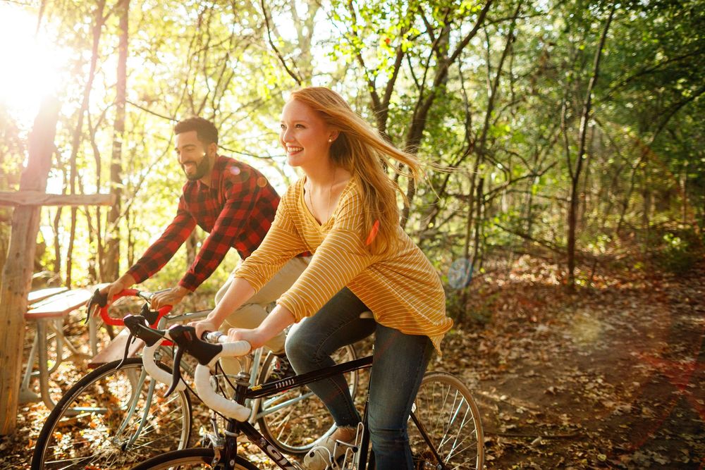 Couple riding bicycles together through a sunny autumn forest trail, smiling and enjoying an outdoor adventure.