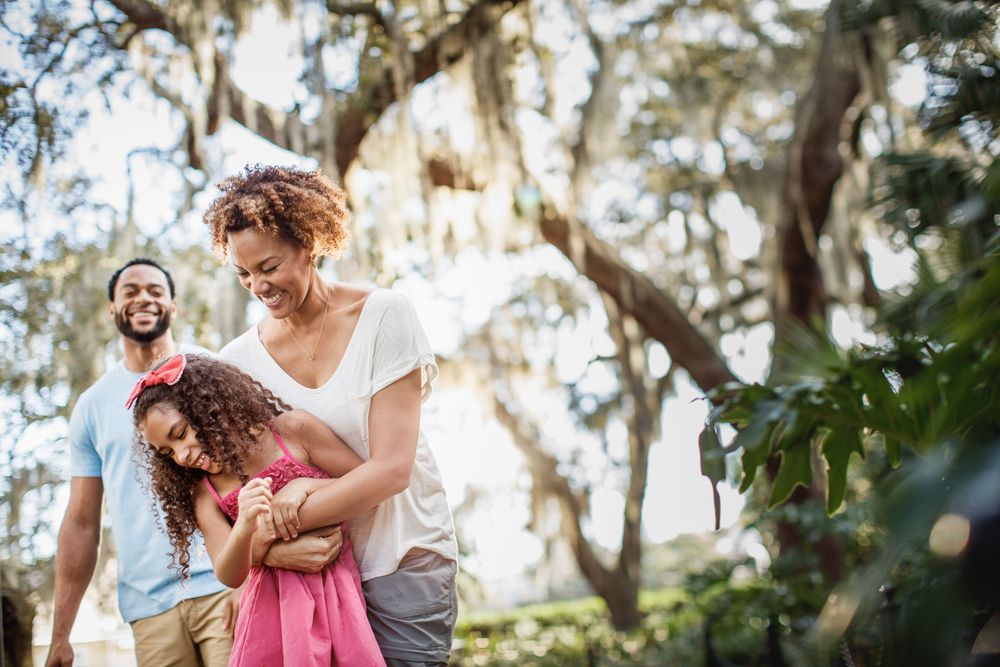 Happy family with a young girl walking outdoors among trees with Spanish moss.