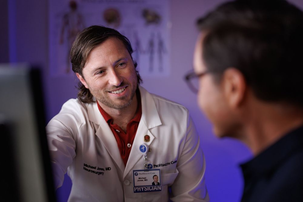 Smiling male physician in white coat consulting with a patient in a medical office setting.