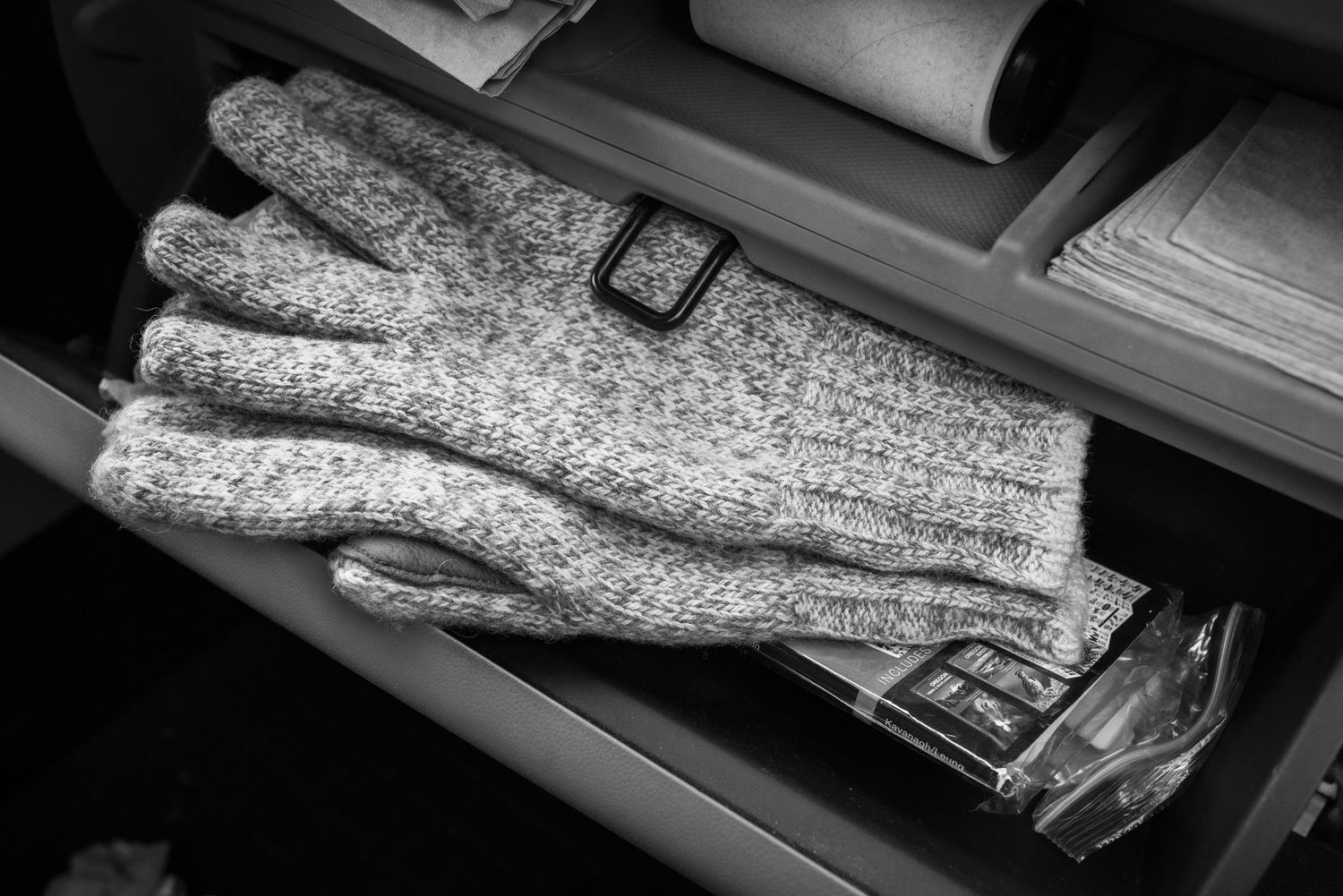 Black and white photo of a knitted wool glove resting inside an open car glove compartment drawer.