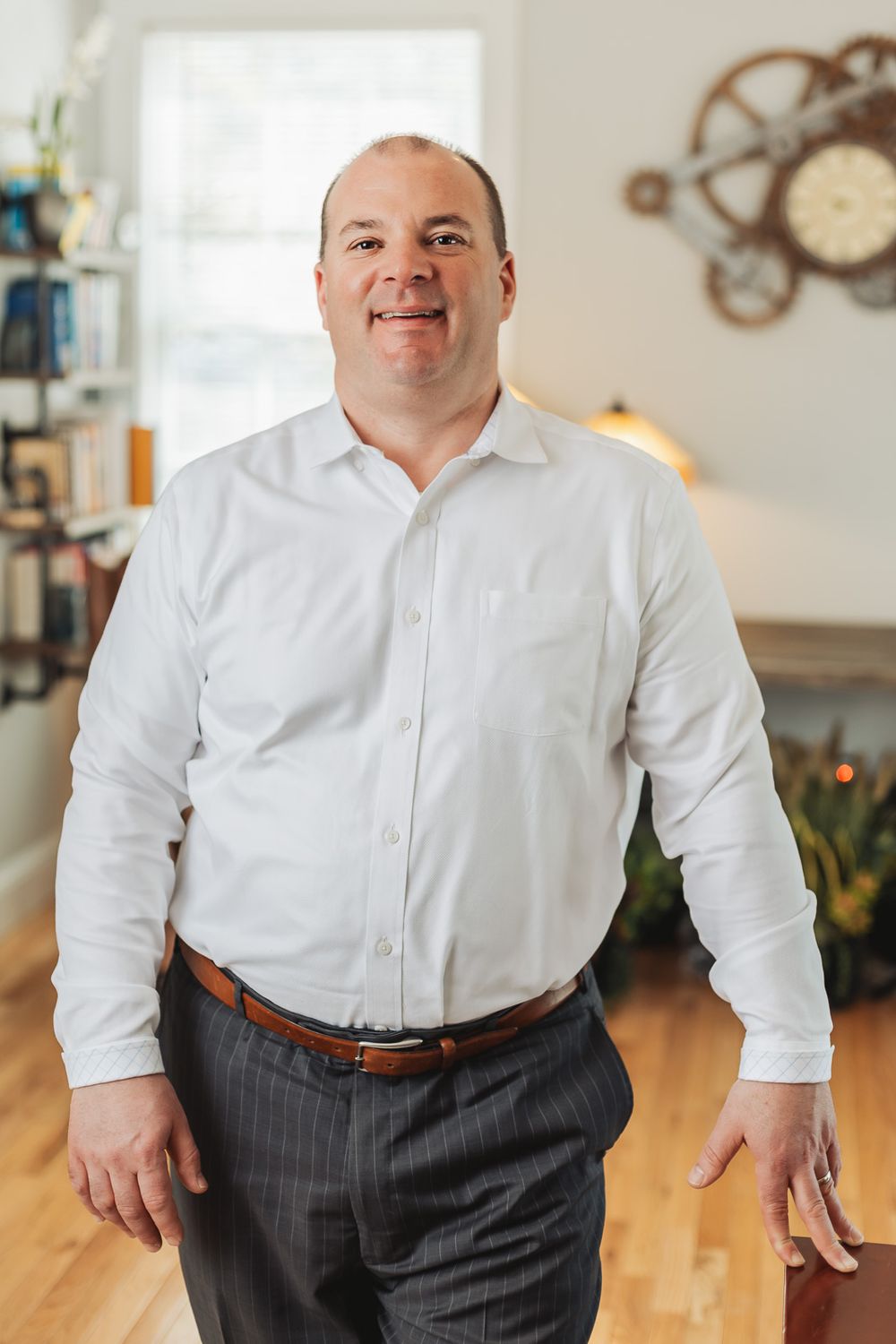 Professional man in white dress shirt and gray slacks smiling confidently in a modern home office setting.