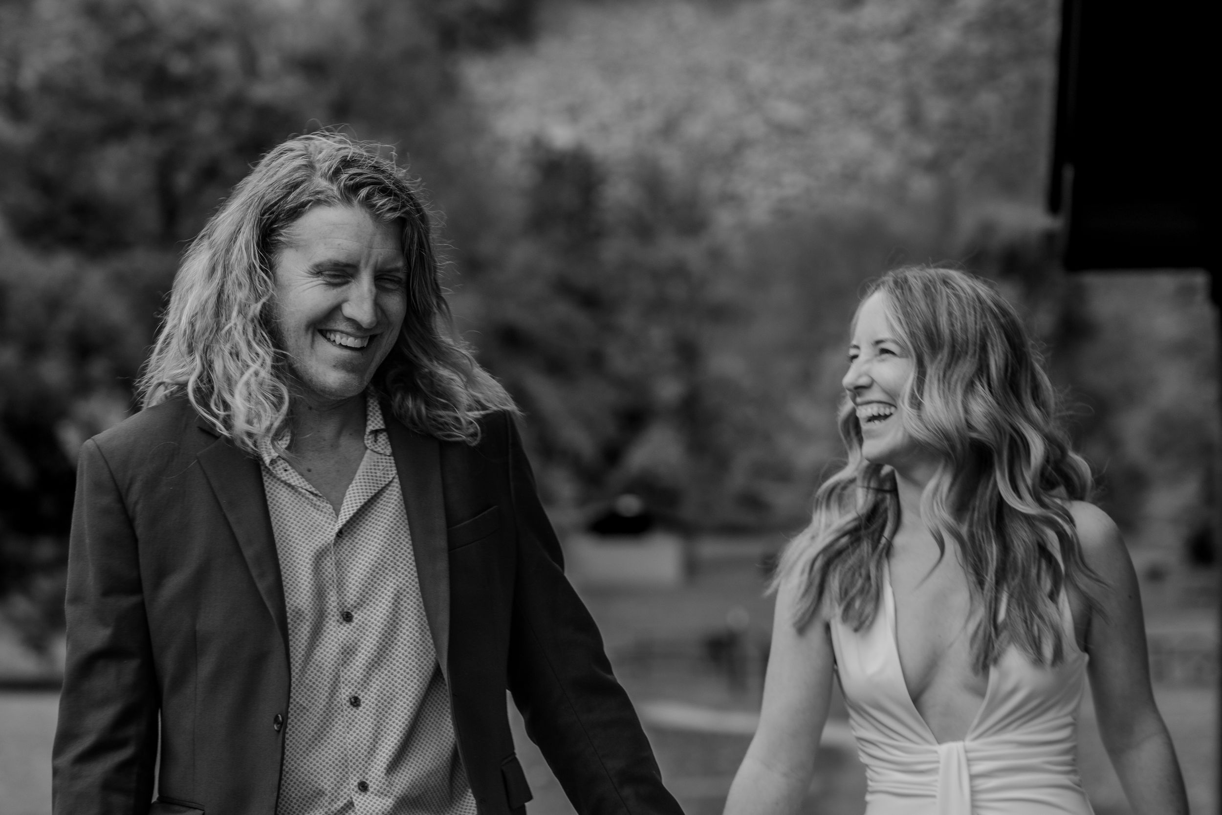Black and white photo of a smiling couple in wedding attire walking together outdoors.