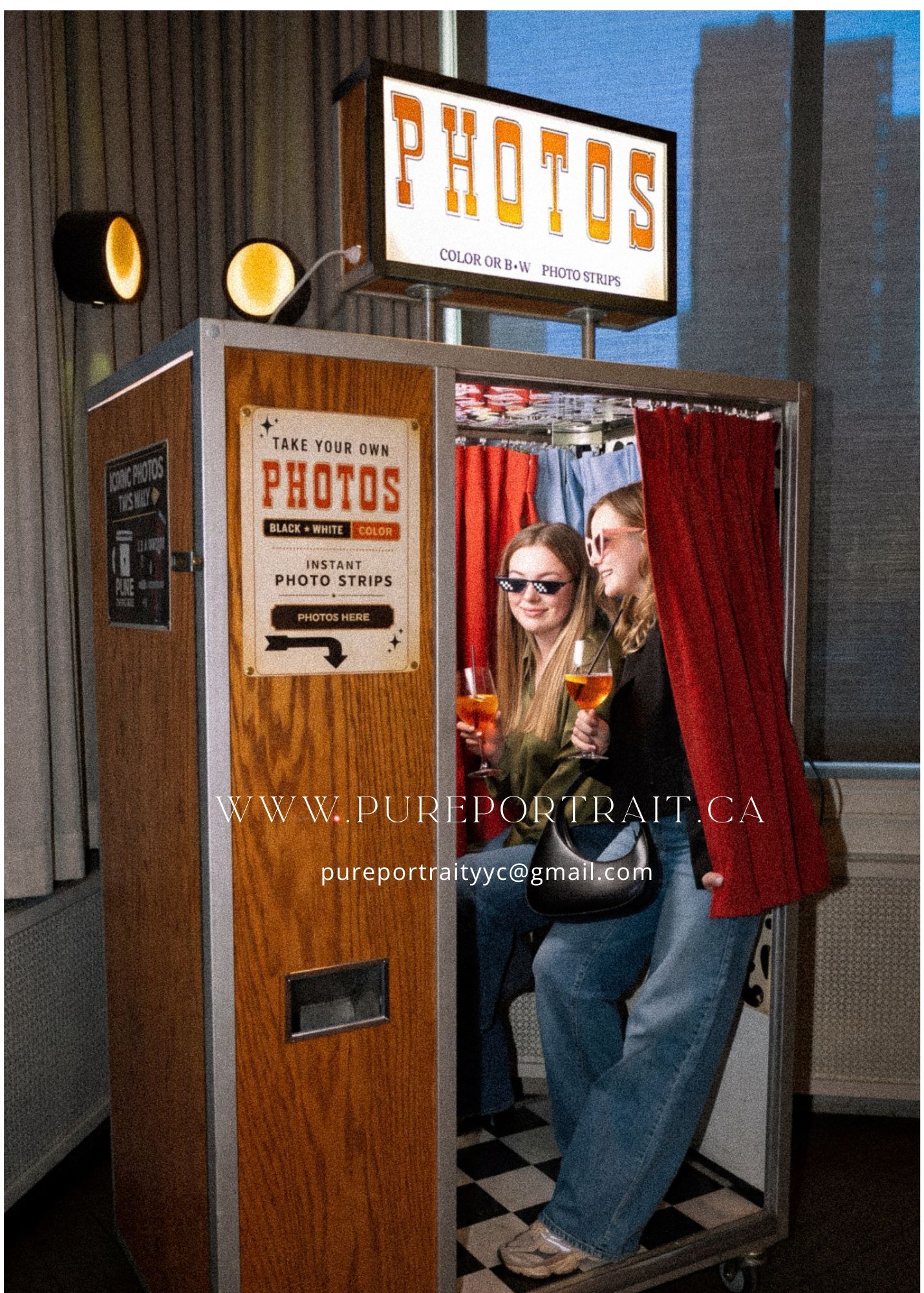 Two women pose inside a vintage wood-paneled photo booth with red curtain at pureportrait.ca event.