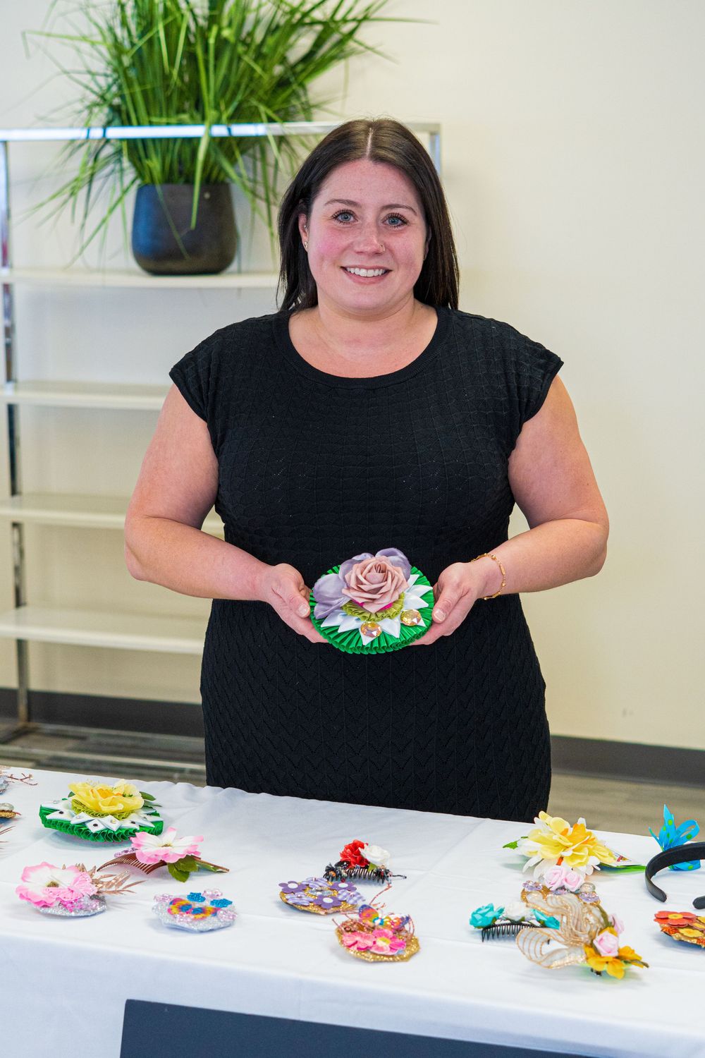 Woman in black dress displays handmade floral hair accessories on a table at a craft showcase.