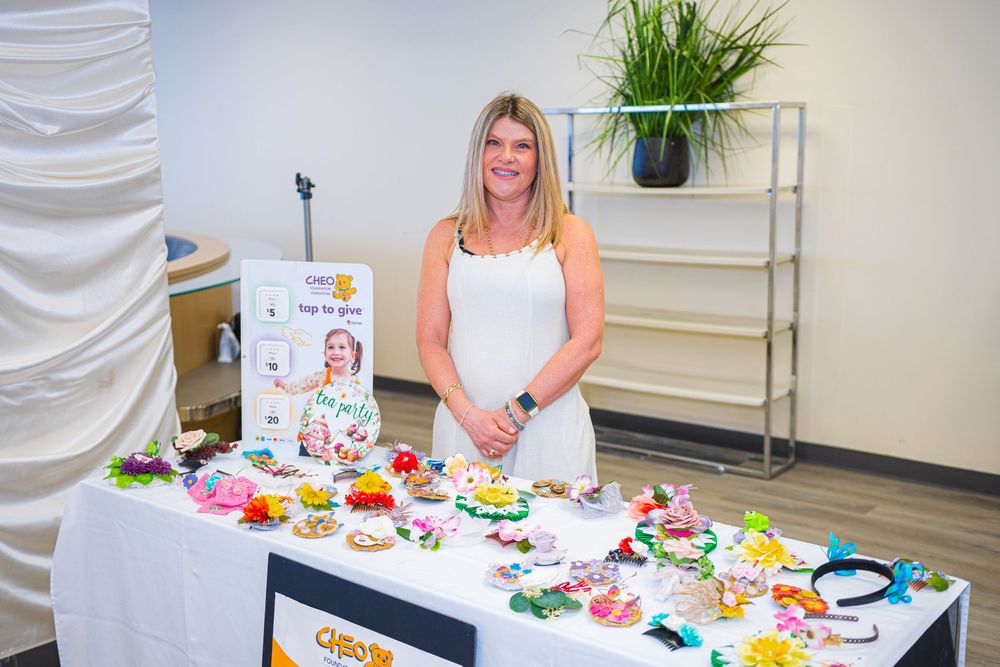 Woman smiling behind a table displaying colorful handmade hair accessories at a vendor booth event.
