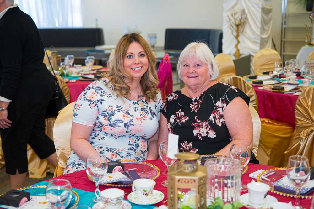 Two women smiling together at an elegantly decorated banquet table with floral teacups and festive decor.