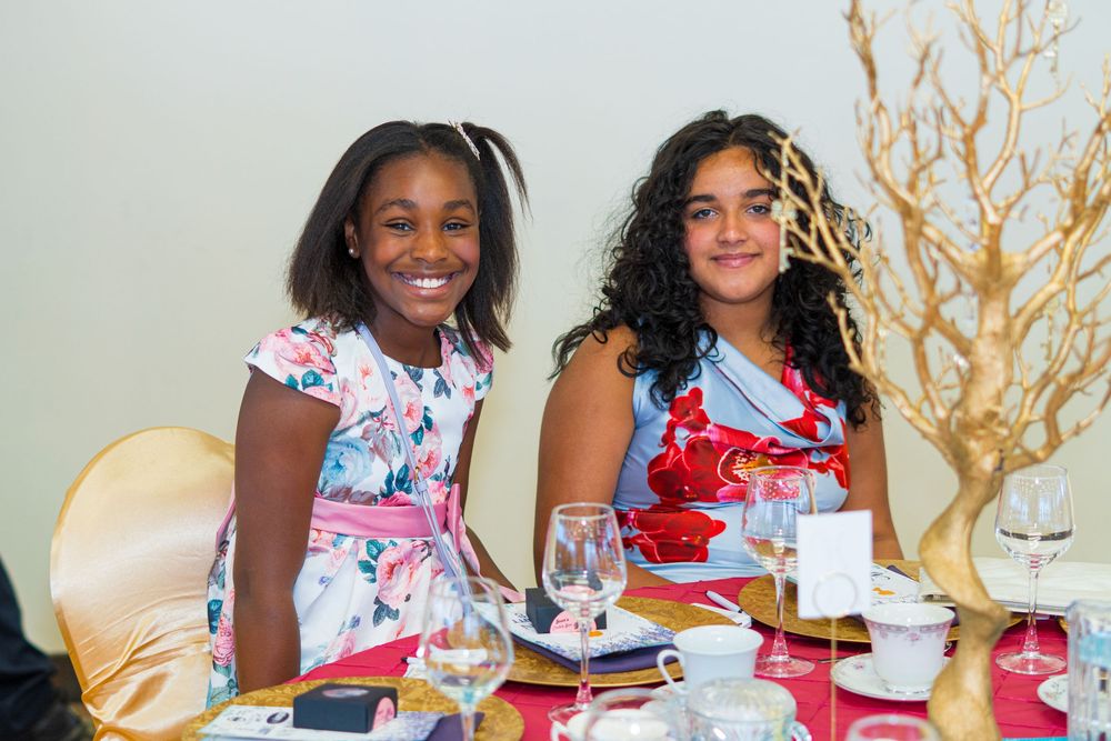 Two young girls smiling at a elegantly decorated banquet table with gold tree centerpiece and pink tablecloth.