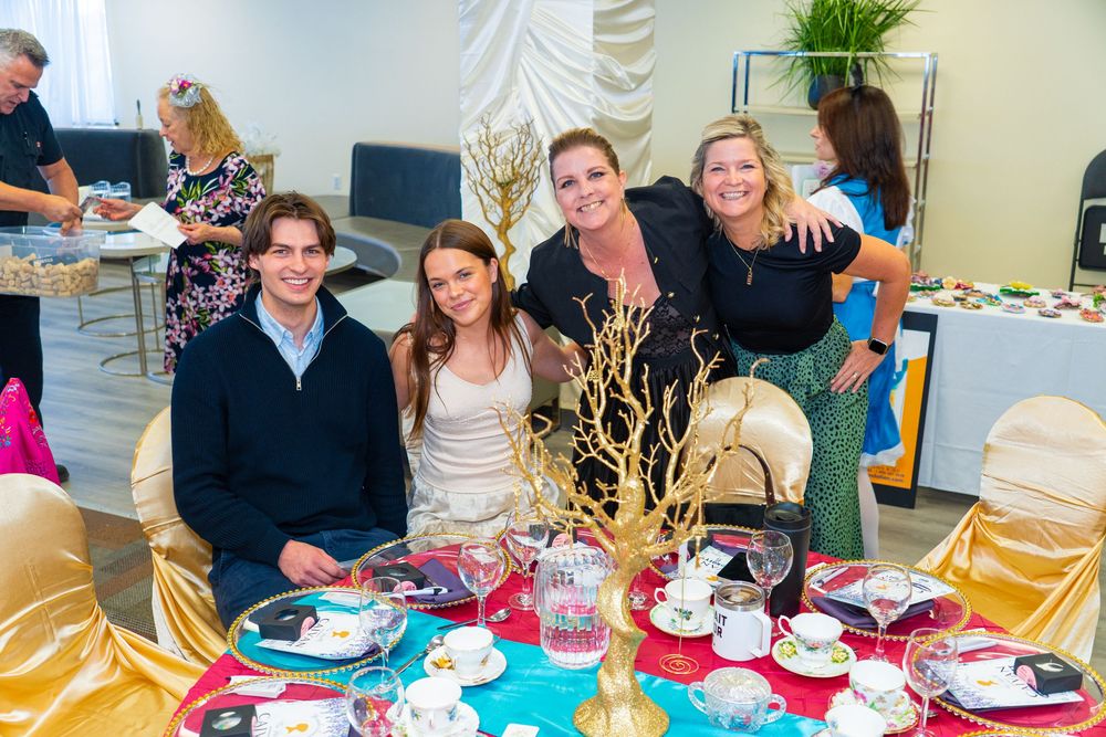 Four friends pose at a decorated table with gold centerpiece at an elegant tea party event.