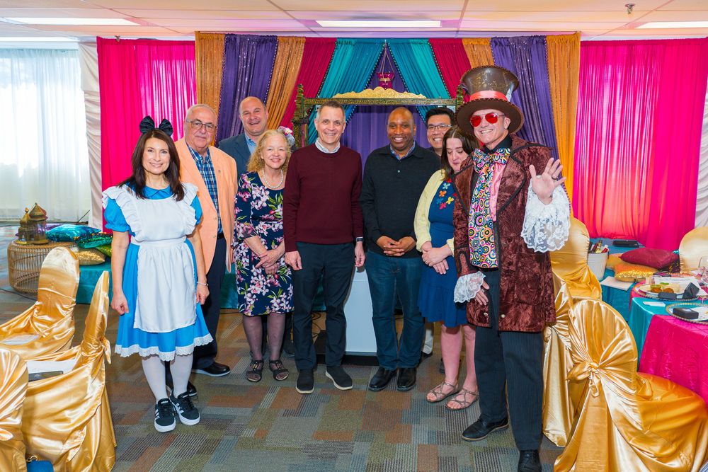 Group photo at Alice in Wonderland themed party with Mad Hatter and Alice characters in decorated venue.