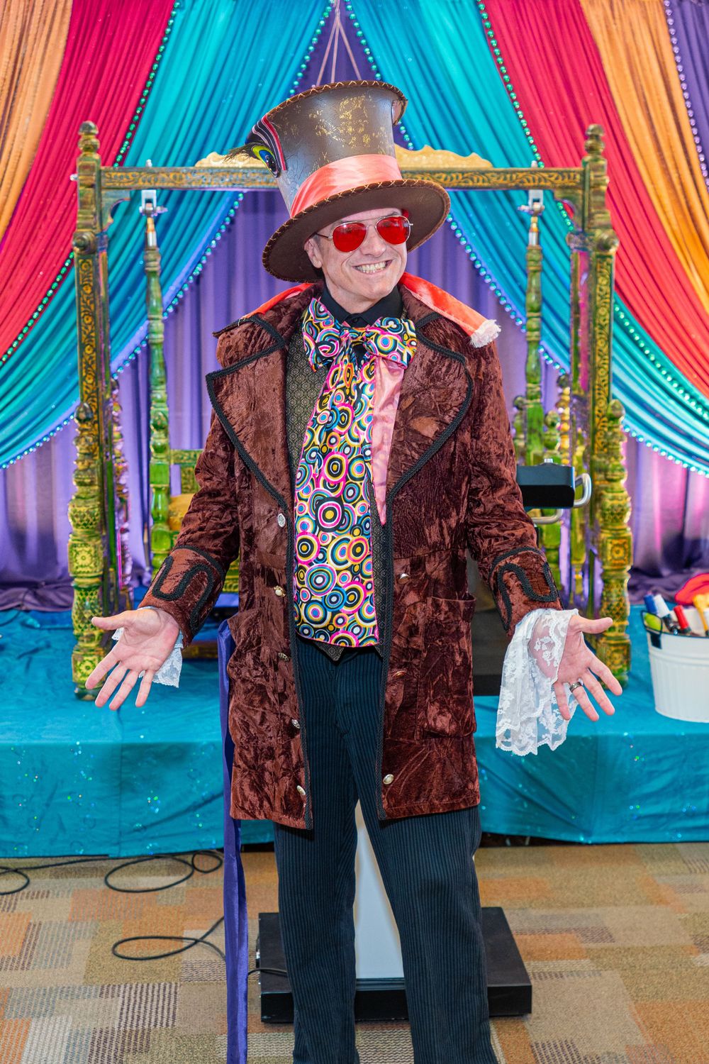 Man dressed as Willy Wonka in top hat, velvet coat, and colorful shirt at a themed party event.