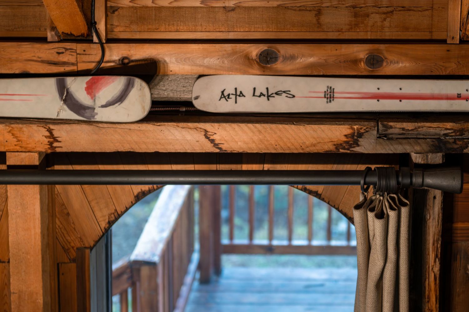 Rustic wooden cabin interior with vintage water skis labeled Alta Lakes mounted above a doorway leading to a deck.