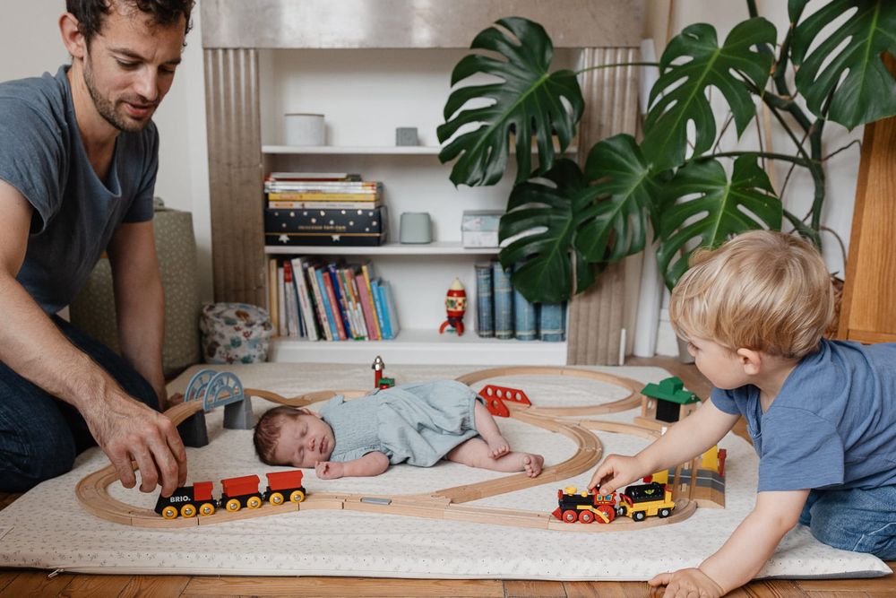 papa joue au petit train avec son fils pendant que la petite soeur est endormie en seance photo de famille a domicile a Lille