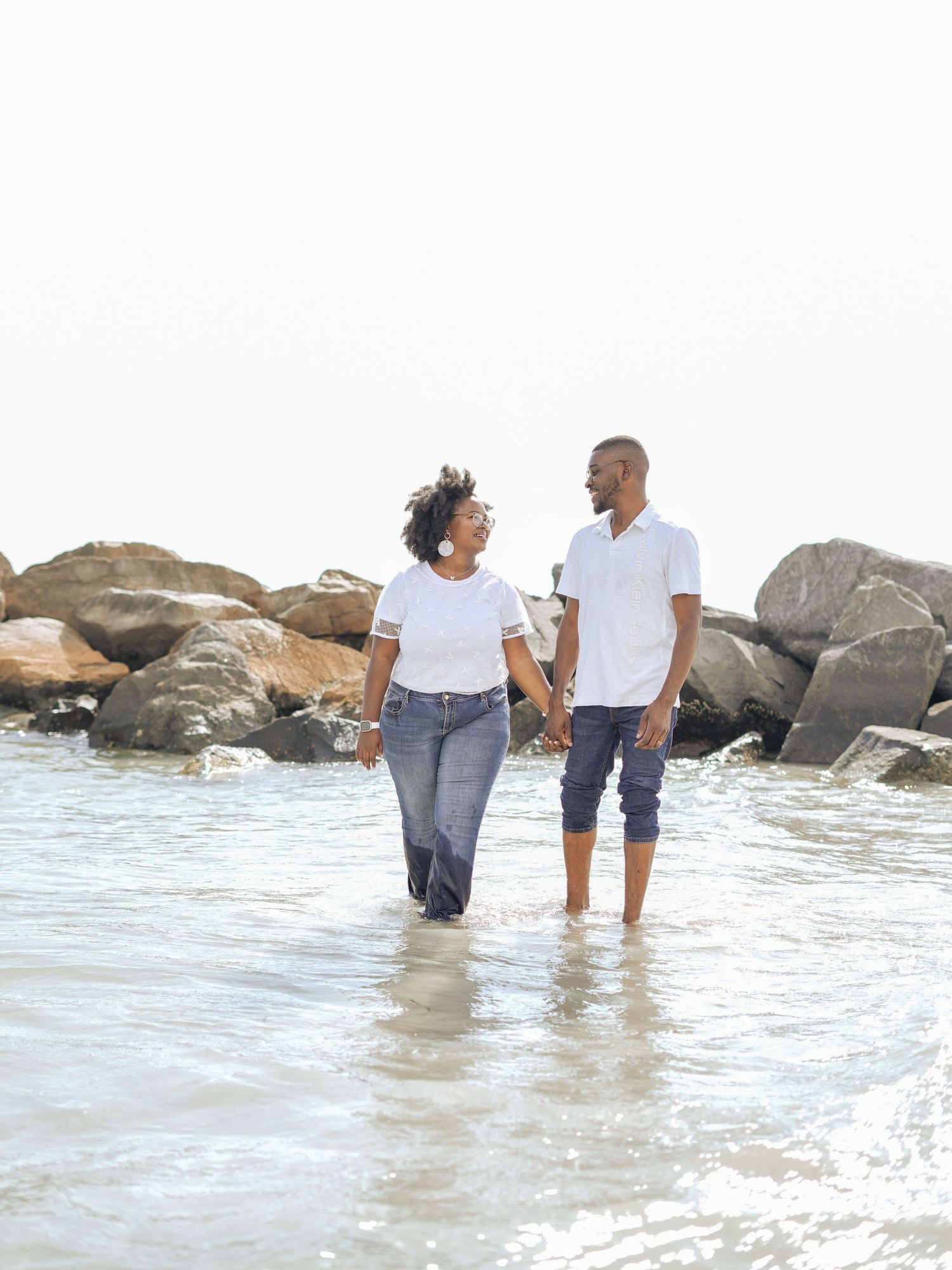 Happy young Black couple embracing outdoors, smiling joyfully against a bright sky backdrop.