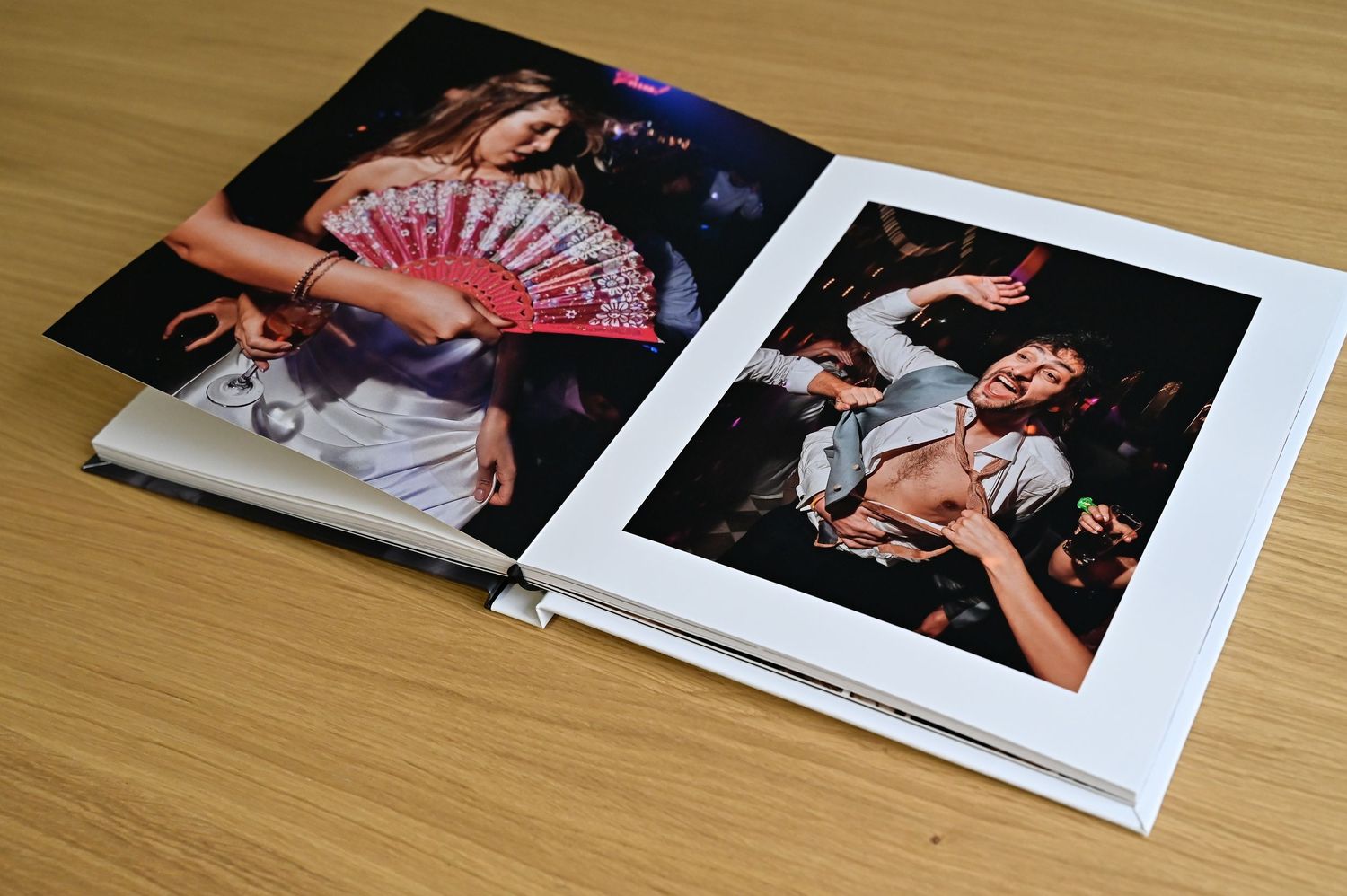 Open hardcover photo book showing vibrant party photography prints on white pages.