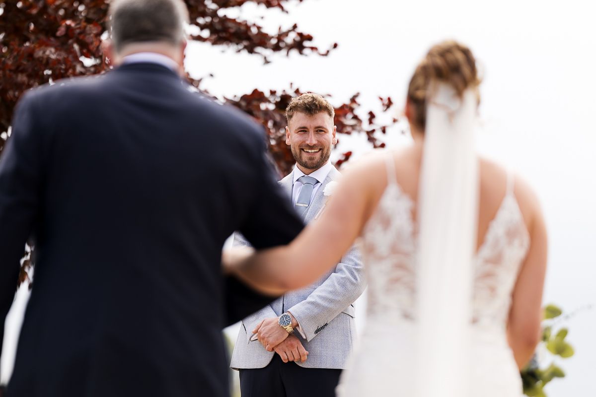Outdoor wedding ceremony with bride and groom holding hands at rustic altar beneath a red tree.