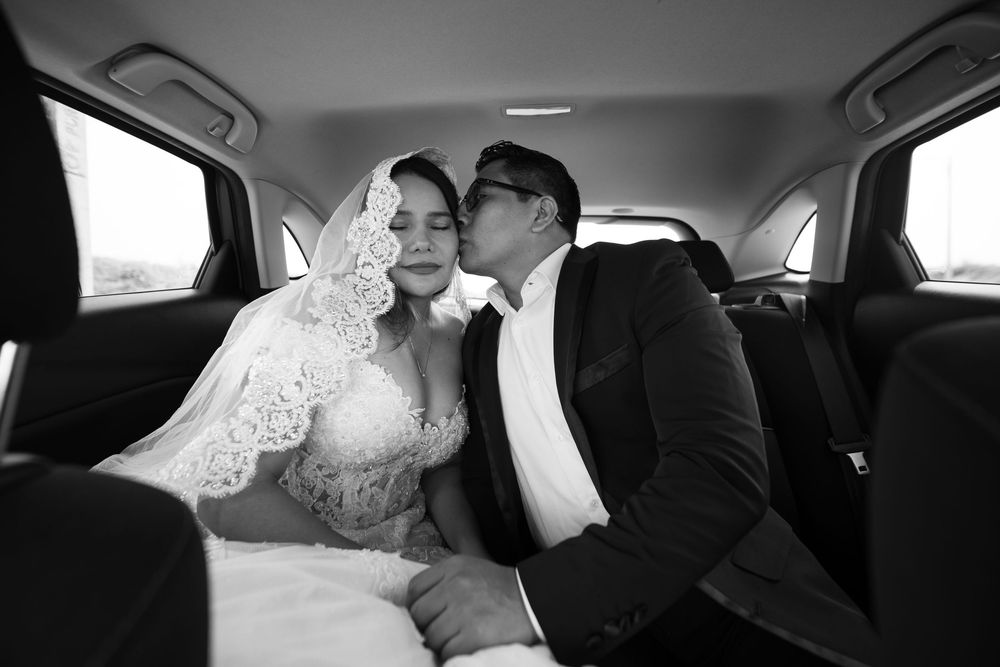 Black and white photo of a bride and groom sharing a tender moment in the backseat of a car on their wedding day.