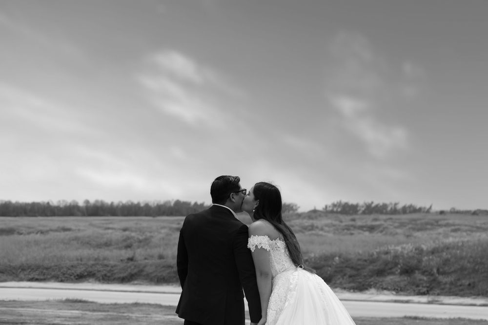 Black and white photo of a couple sharing a kiss outdoors on their wedding day, bride in white gown.