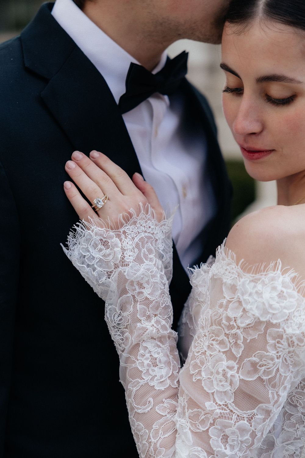 Close-up of bride in lace wedding gown displaying diamond ring on her hand.