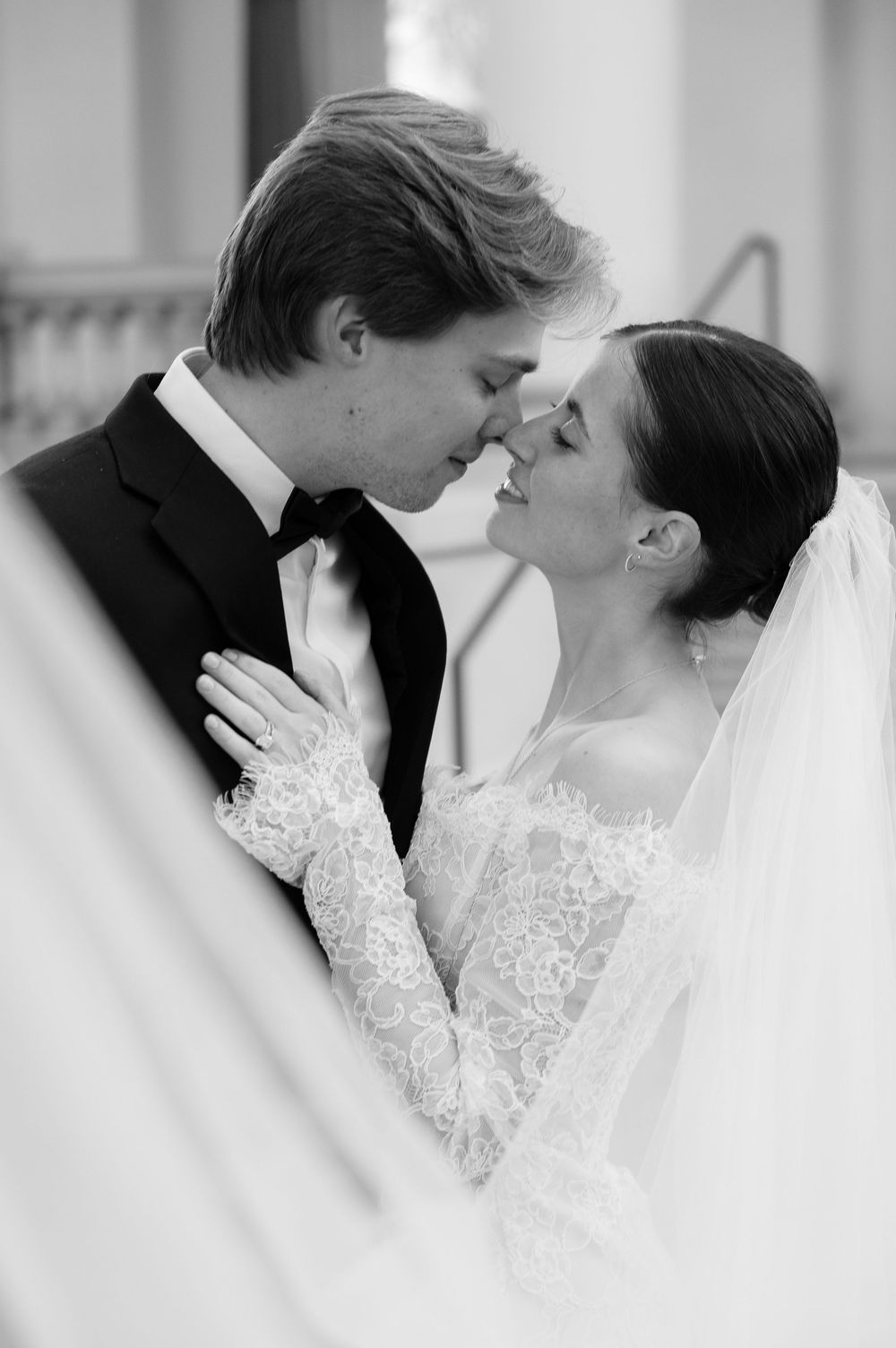 Black and white romantic portrait of bride and groom nearly kissing in lace wedding attire.
