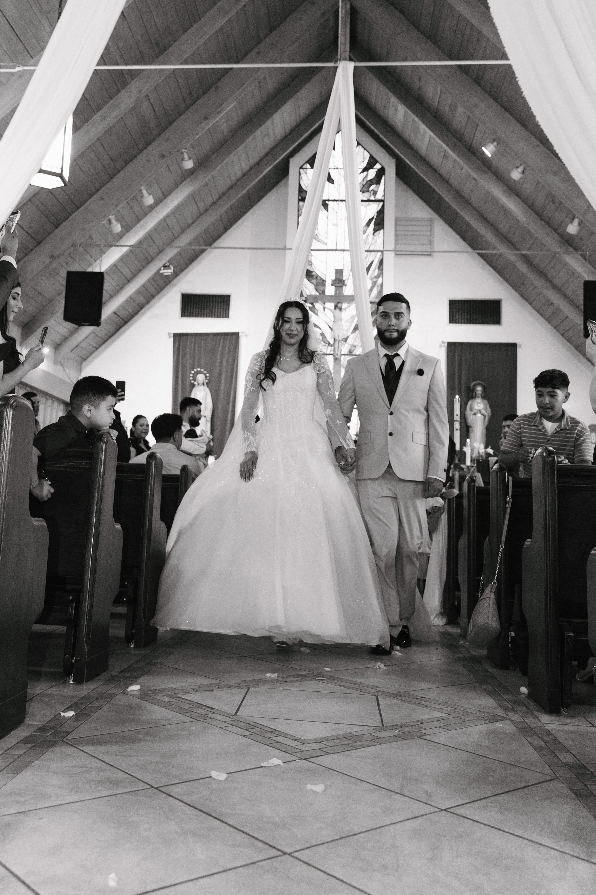 Black and white photo of a bride and groom walking down the aisle of a church after their wedding ceremony.