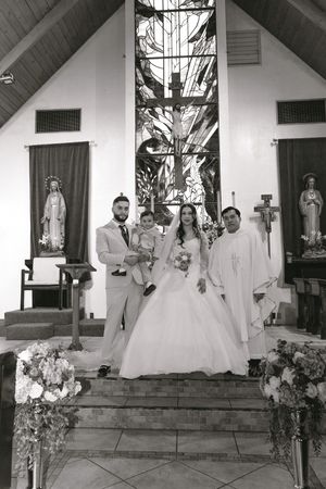 Black and white photo of bride and groom with child and priest at church altar after wedding ceremony.