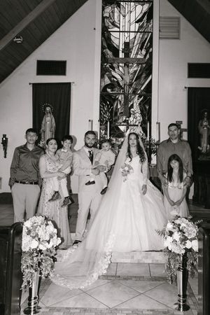 Black and white wedding photo of bride, groom, and family posing at church altar after ceremony.