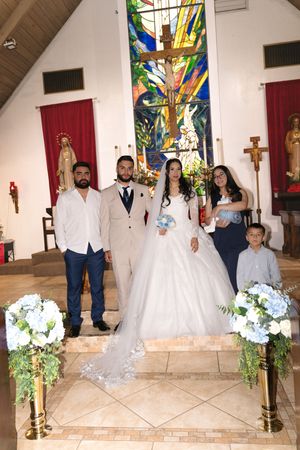 Bride and groom pose with family members at church altar with colorful stained glass window backdrop.