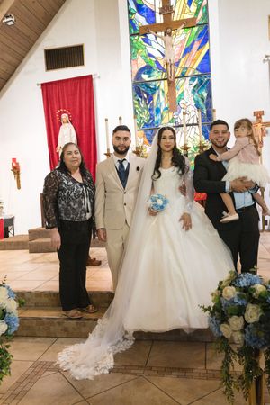 Bride and groom pose with family inside a church after wedding ceremony, with stained glass cross backdrop.