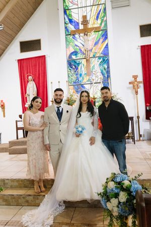 Wedding couple poses with two guests inside a church featuring a vibrant stained glass window.