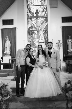 Black and white photo of a bride and groom posing with two guests inside a decorated church after their wedding ceremony.