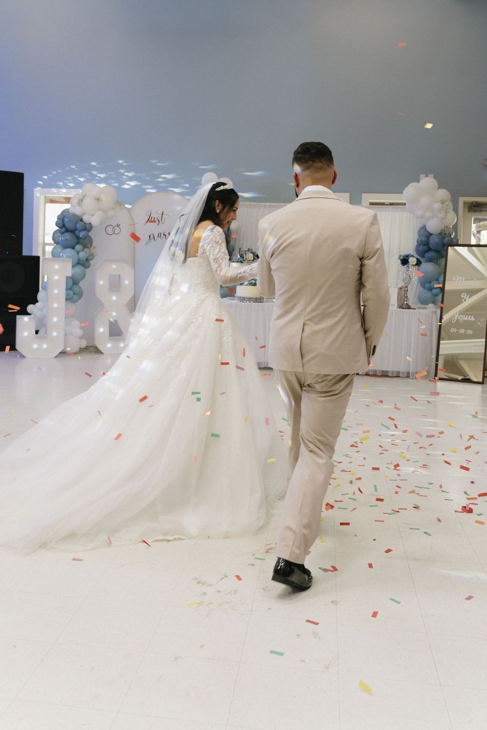 Bride and groom share first dance on confetti-covered floor with balloon arch backdrop at elegant wedding reception.