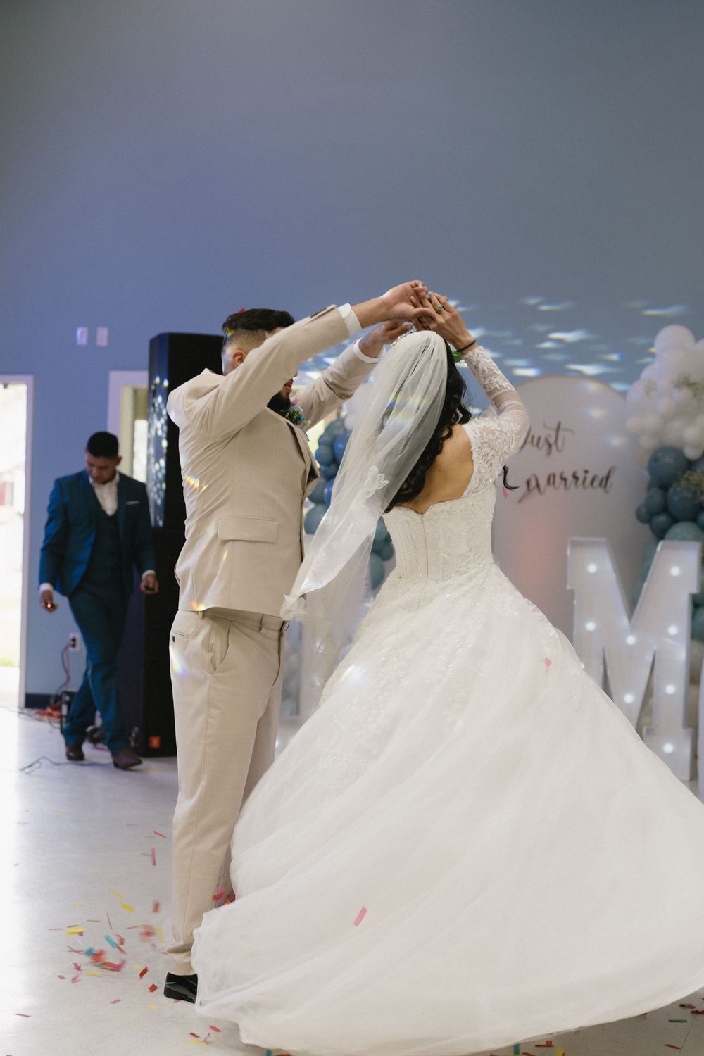 Bride and groom share first dance at wedding reception with Just Married balloon backdrop and confetti falling.