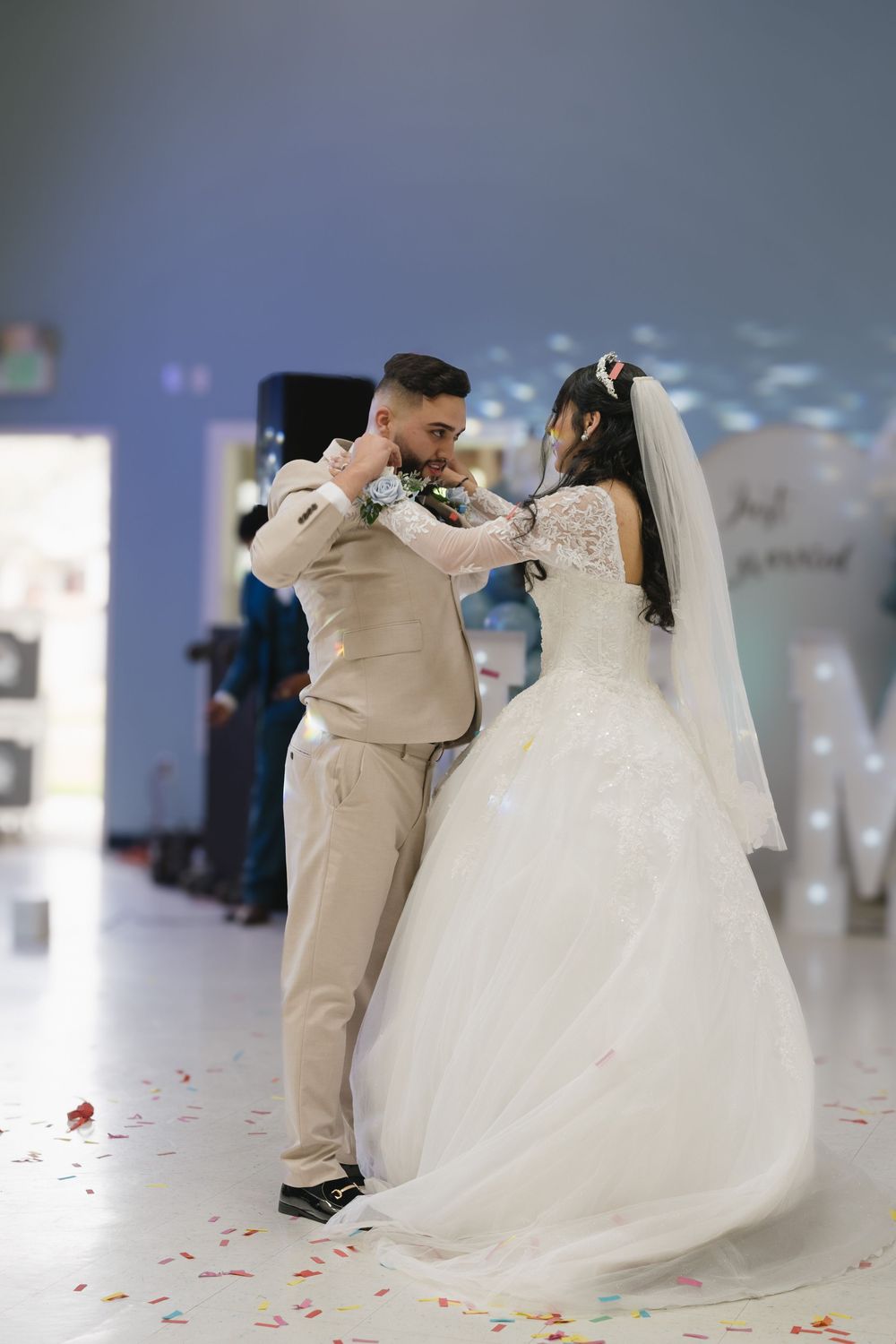 Newlyweds sharing romantic first dance embrace at decorated wedding venue with confetti.