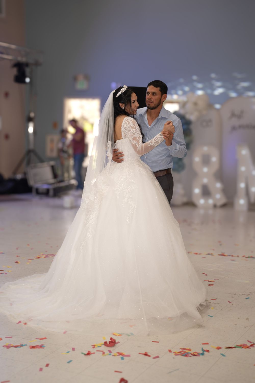 Bride and groom share their first dance, bride wearing elegant white ball gown with lace sleeves and veil.