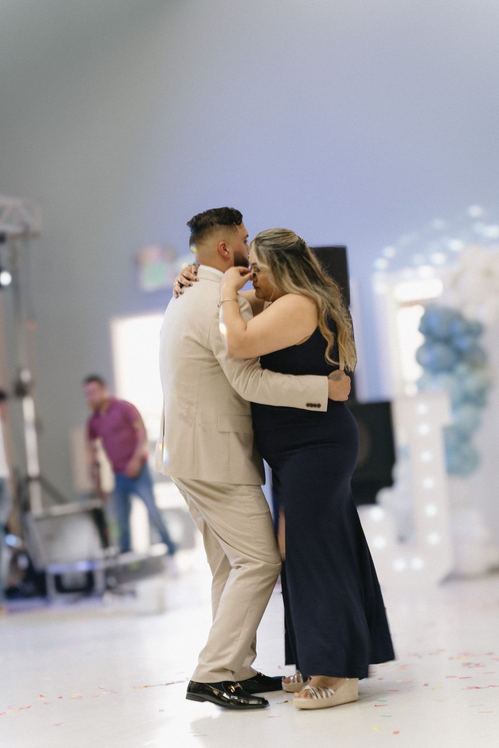 Couple shares a romantic slow dance, man in beige suit and woman in black dress at a formal event.