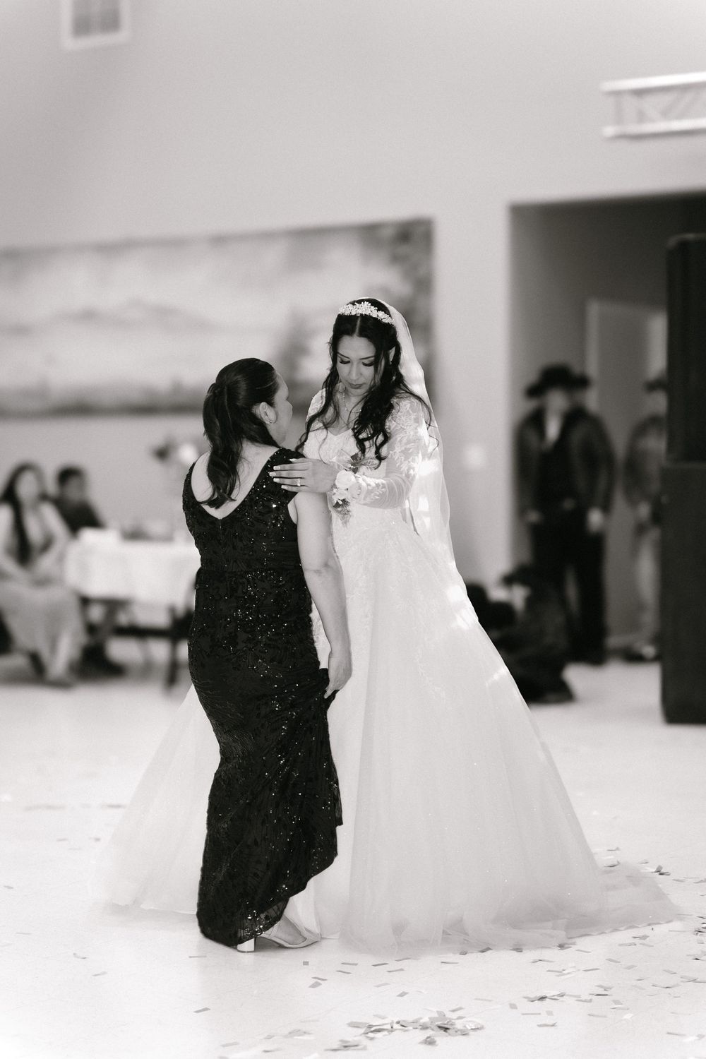 Black and white photo of bride in lace gown sharing tender mother-daughter dance at wedding.
