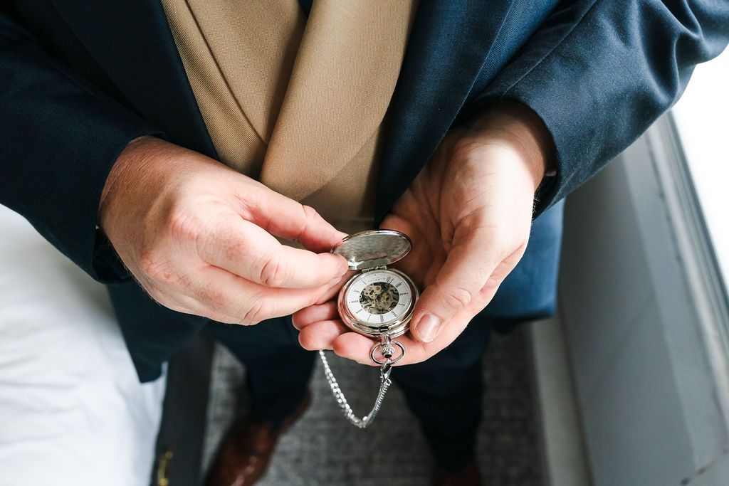 Person in suit holding open silver pocket watch with chain, close-up detail shot.