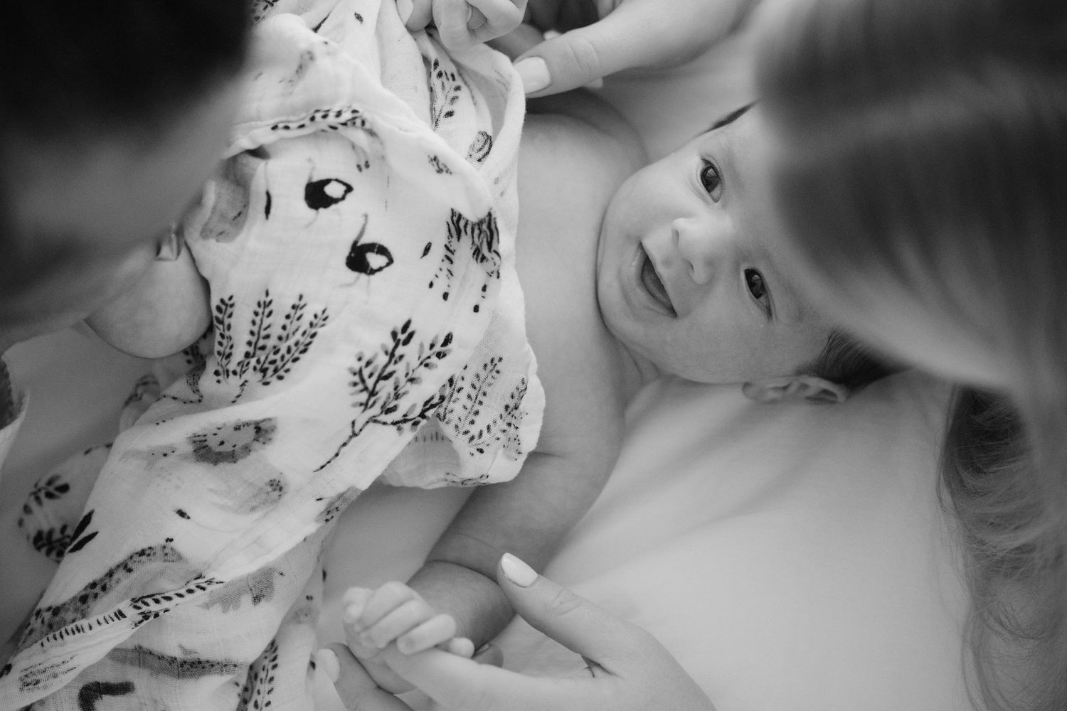 Black and white photo of happy newborn baby framed by mother and father during newborn session Vancouver