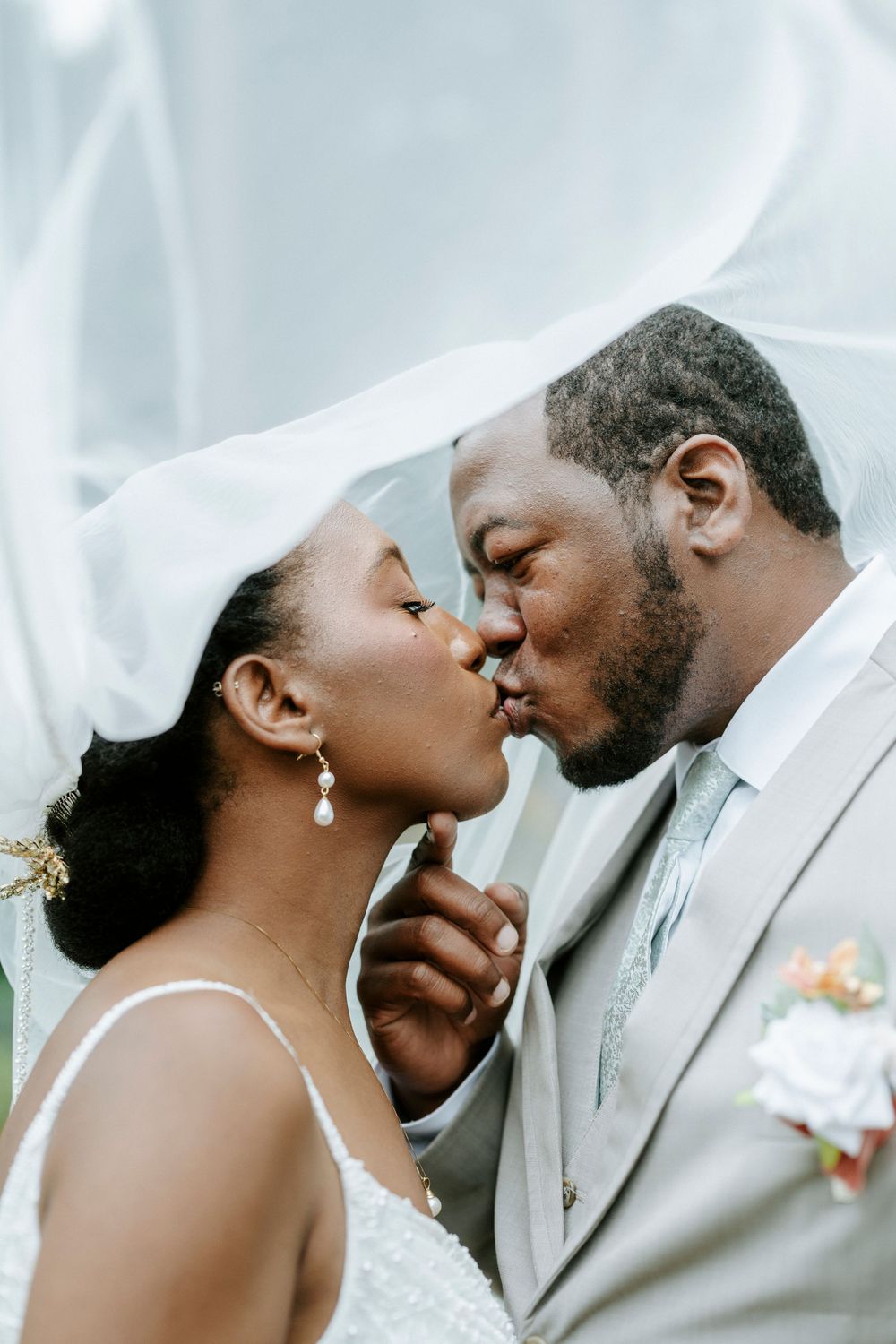 A Black bride and groom share a romantic kiss under a white veil on their wedding day.