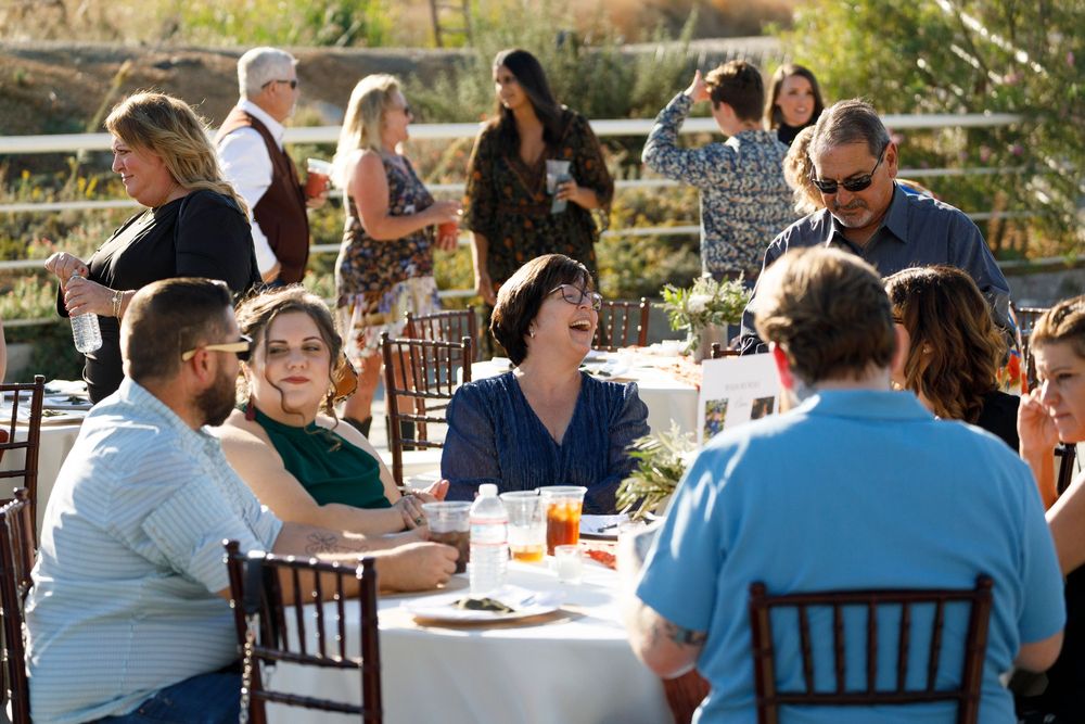 Guests enjoy an outdoor dining event at a winery, seated at white-clothed tables in warm sunlight.