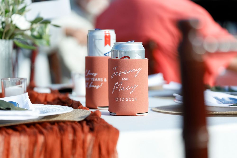 Personalized terracotta wedding koozies for Jeremy and Macy displayed on a decorated reception table with rustic linens.