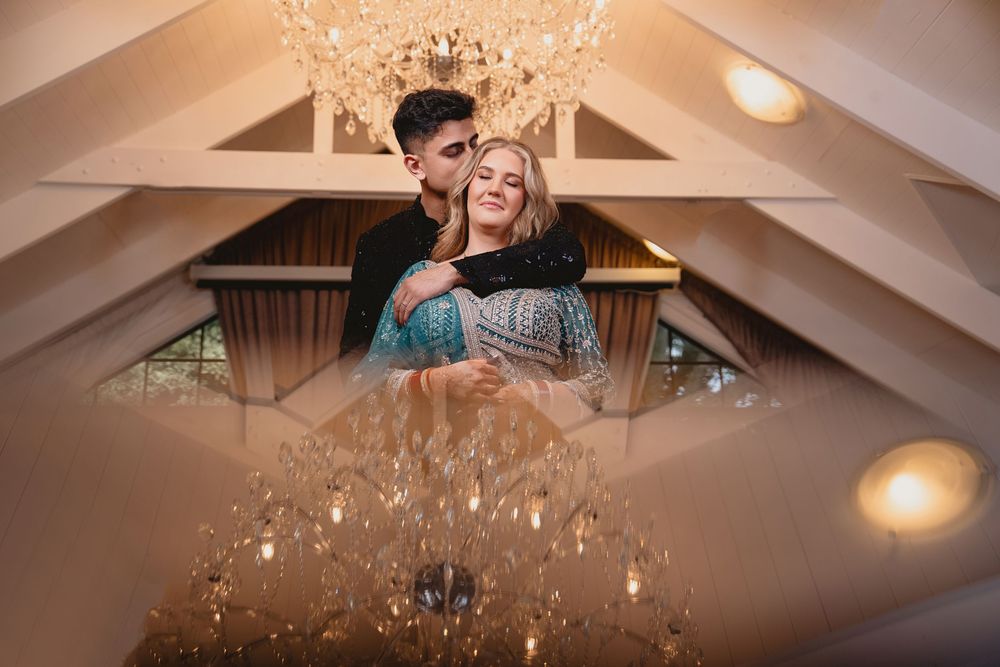 Couple embracing romantically under elegant chandeliers in a warmly lit venue with vaulted ceiling.