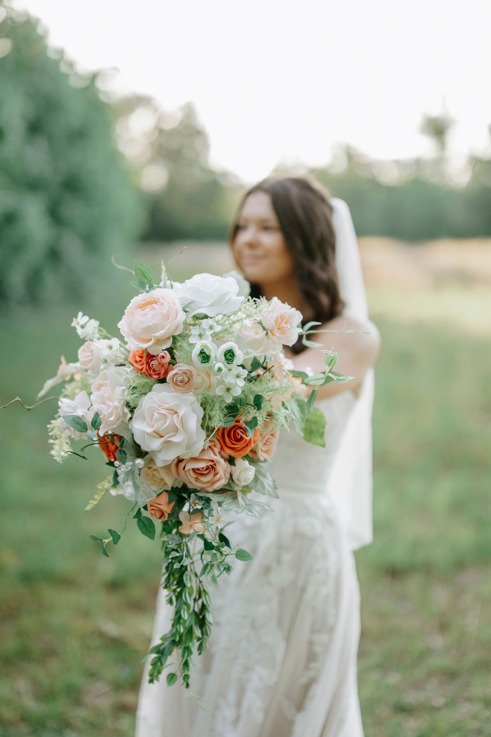 Close-up of lush bridal bouquet with peach, orange, and white roses held by bride outdoors.