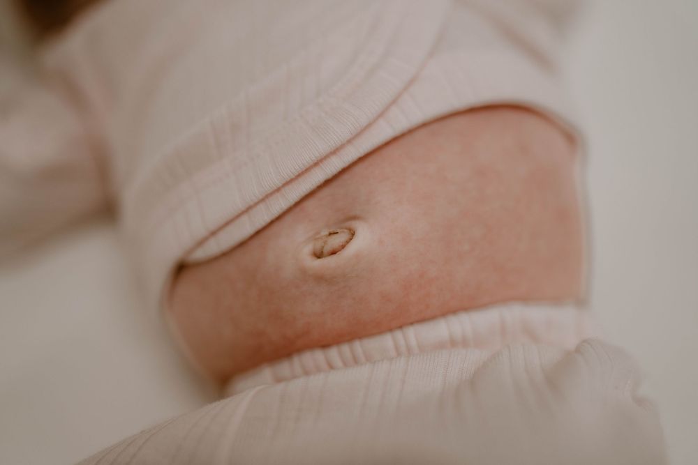 Close-up of a belly button on a newborn baby wearing a soft pink onesie, showing the healing umbilical cord stump.