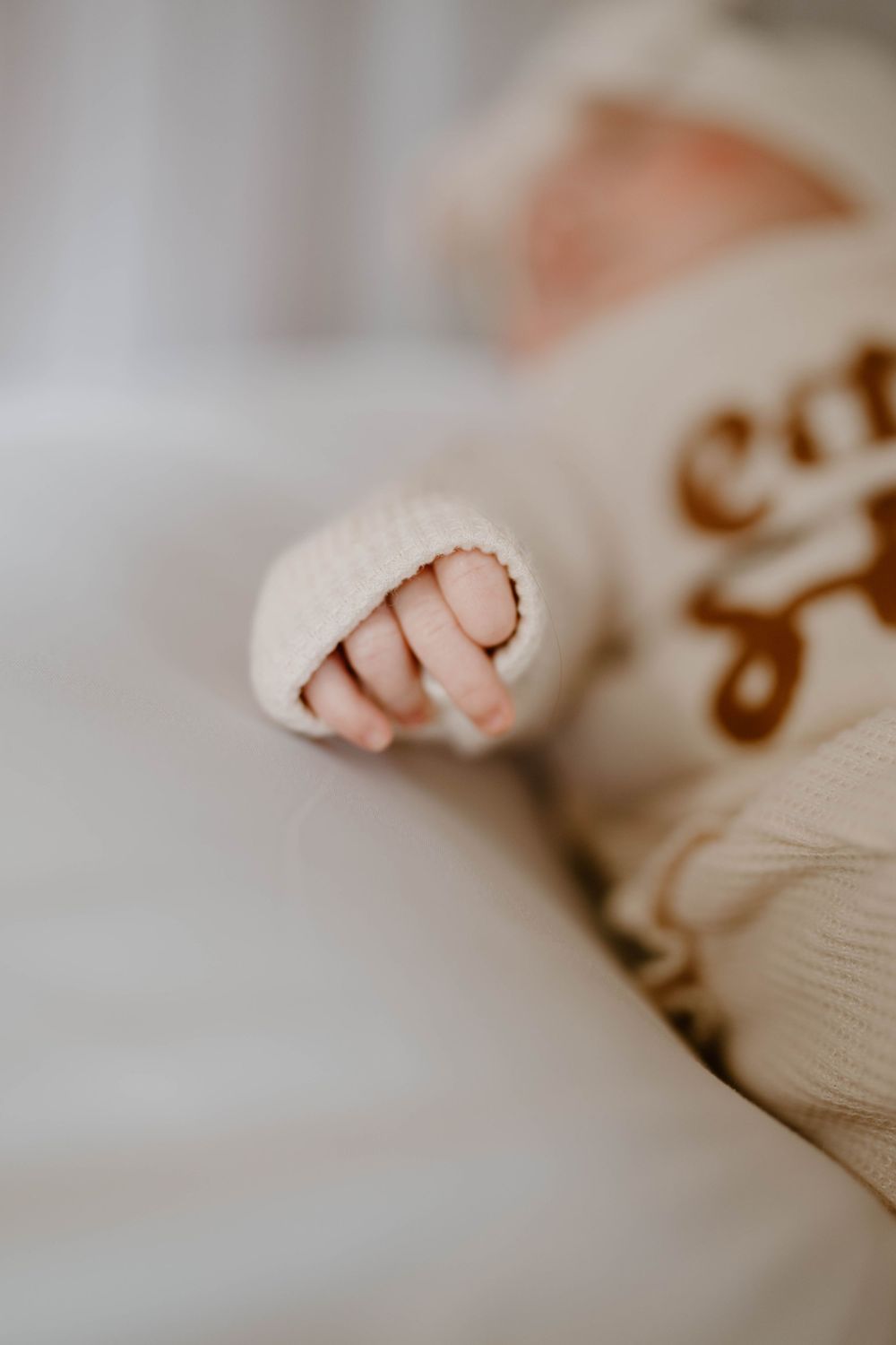 Close-up of a newborn baby's tiny hand peeking out from a cream knit sweater sleeve.