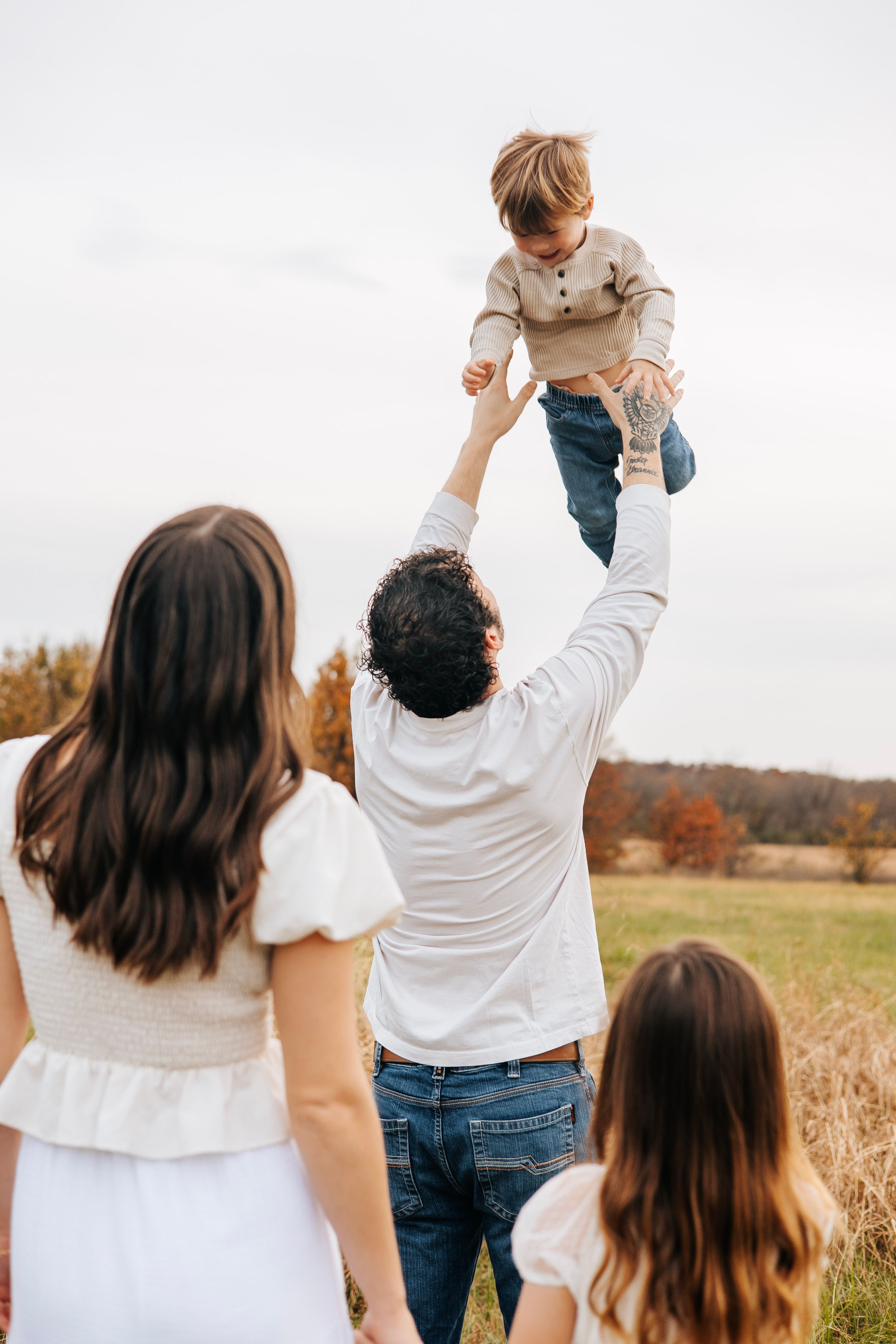 Father tossing young child in air during fall family photo session in golden meadow.