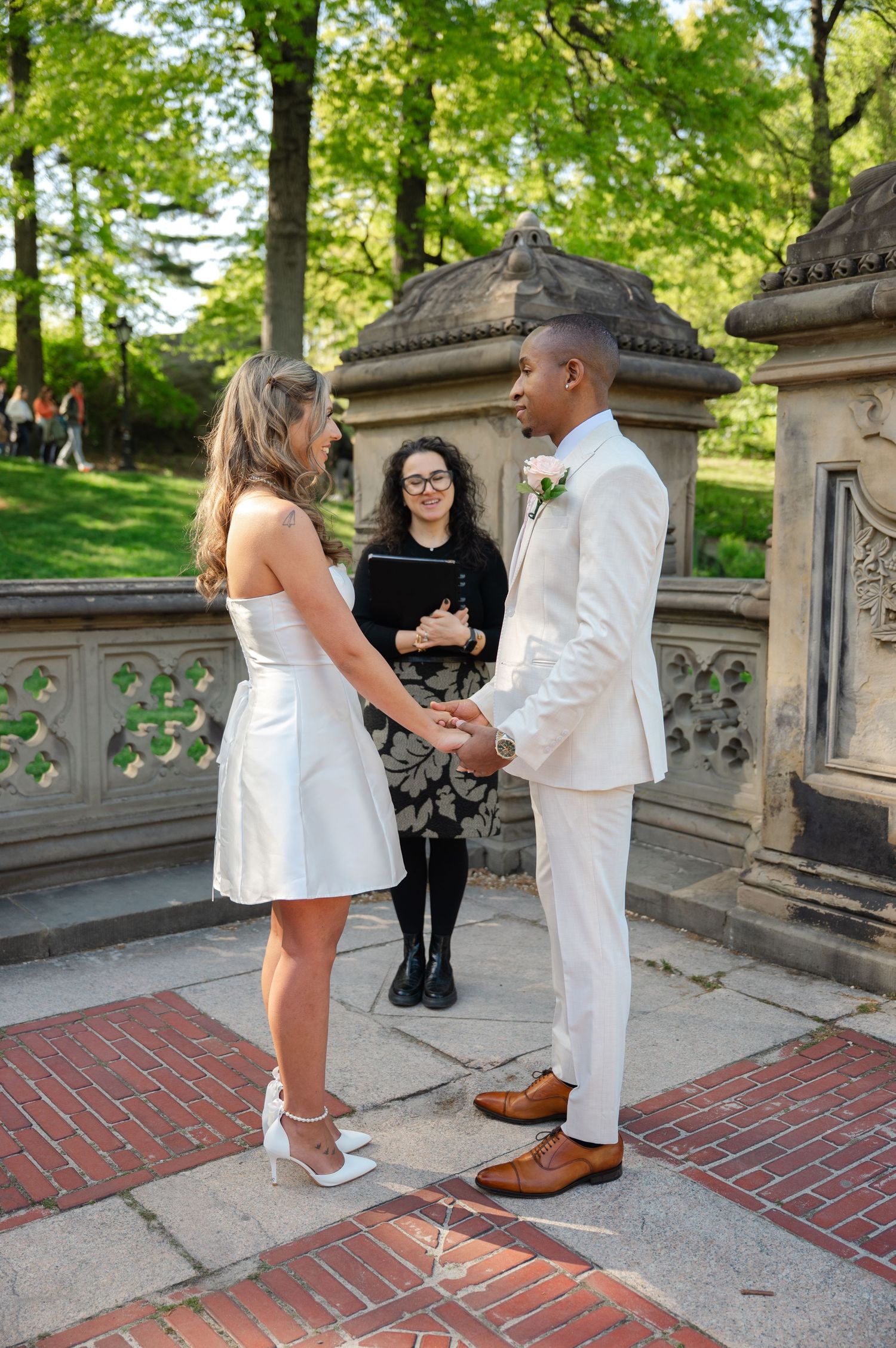 Couple exchanges vows at Bethesda Terrace in Central Park, officiated by a woman in a black dress on a sunny day.