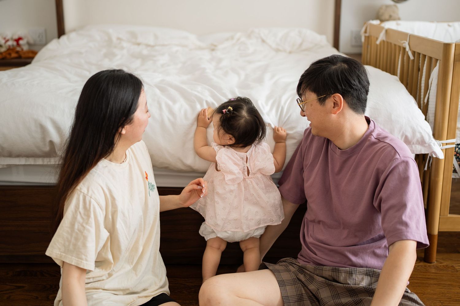 Family spending quality time together in a cozy bedroom setting, with a small child in a pink dress.