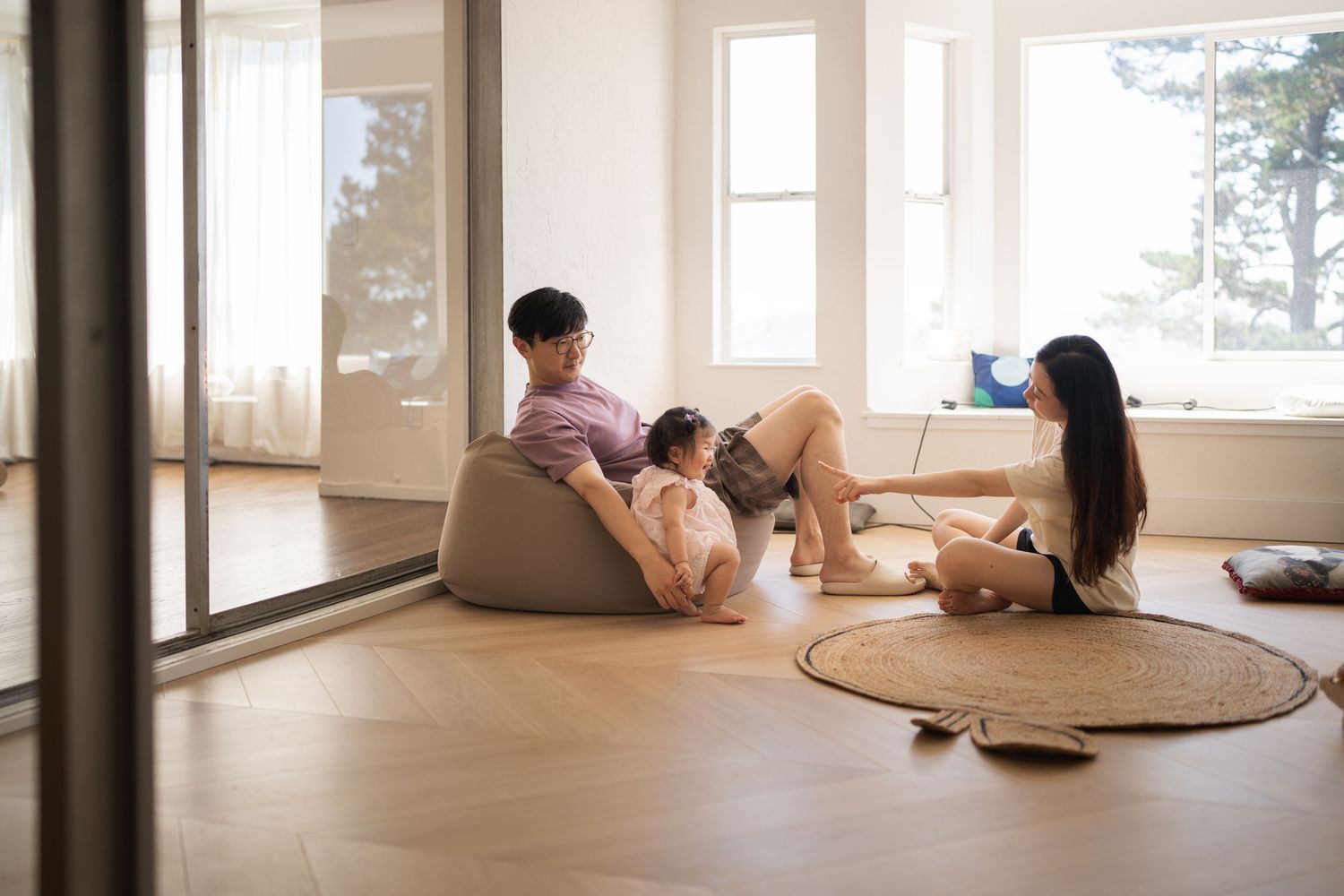 Bright modern room with large windows and people sitting on cushions in a minimalist space.