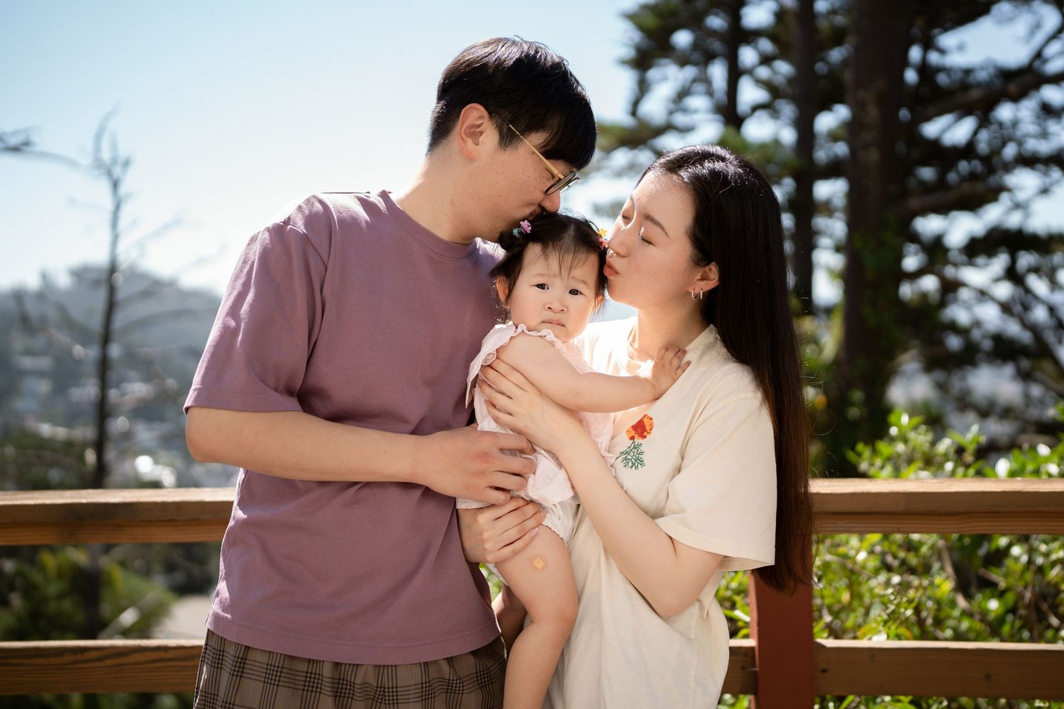A family shares a tender moment together outdoors on a sunny deck surrounded by trees.